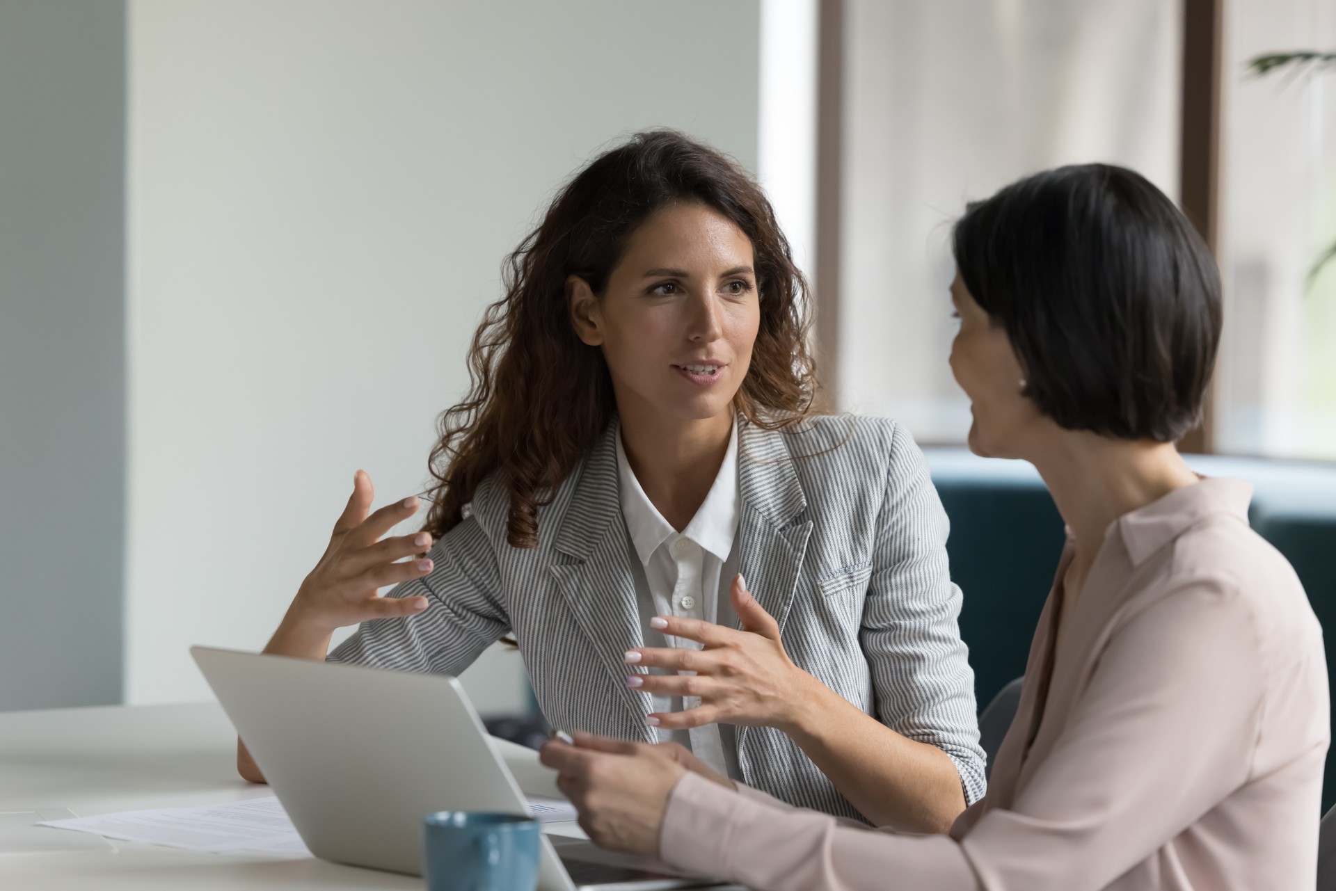 Two attractive businesswomen sit at desk discuss project details